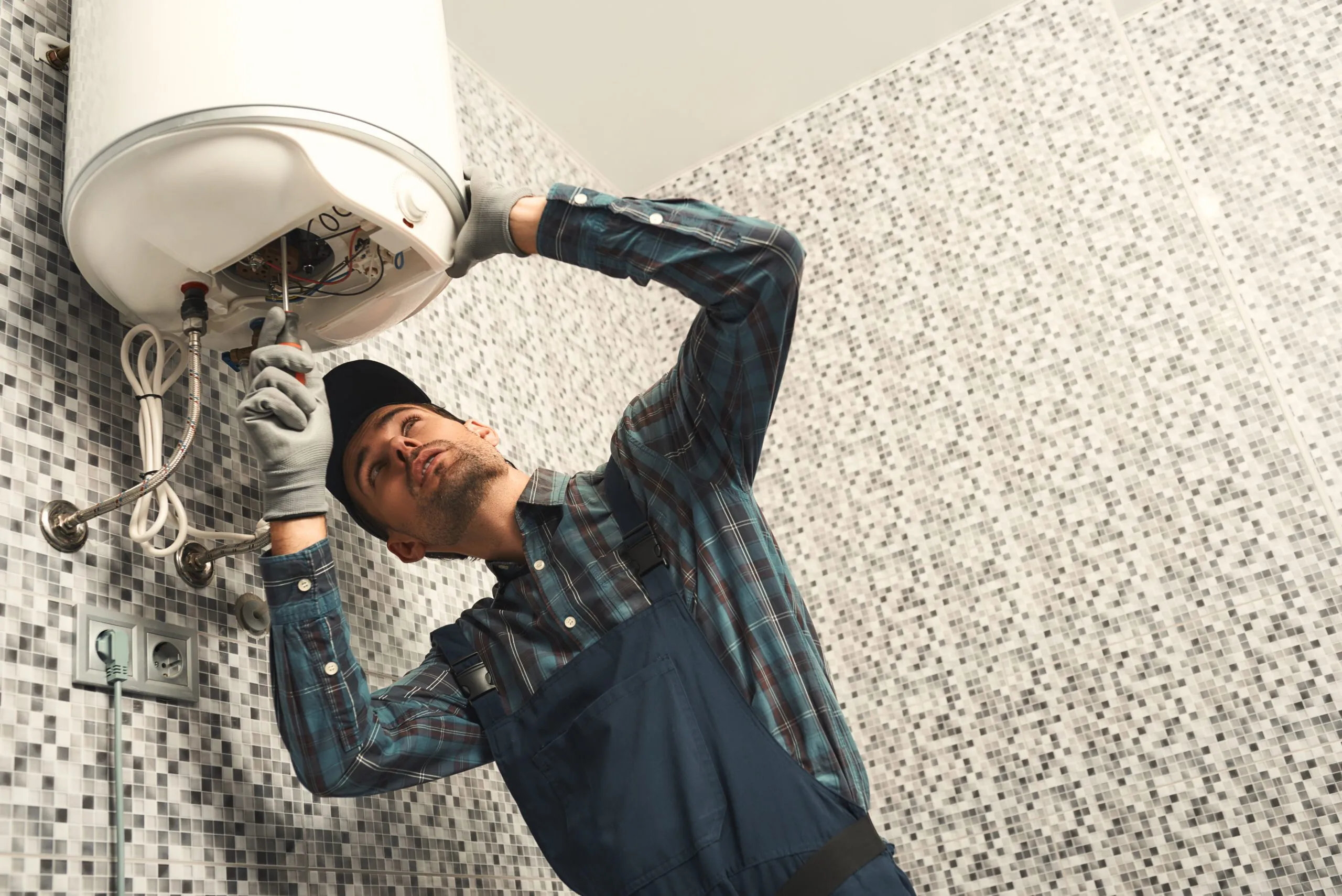 Plumber-installing-electric-heating-boiler.-Young-handyman-in-uniform-setting-up-electric-heating-boiler-at-home-waksdn1